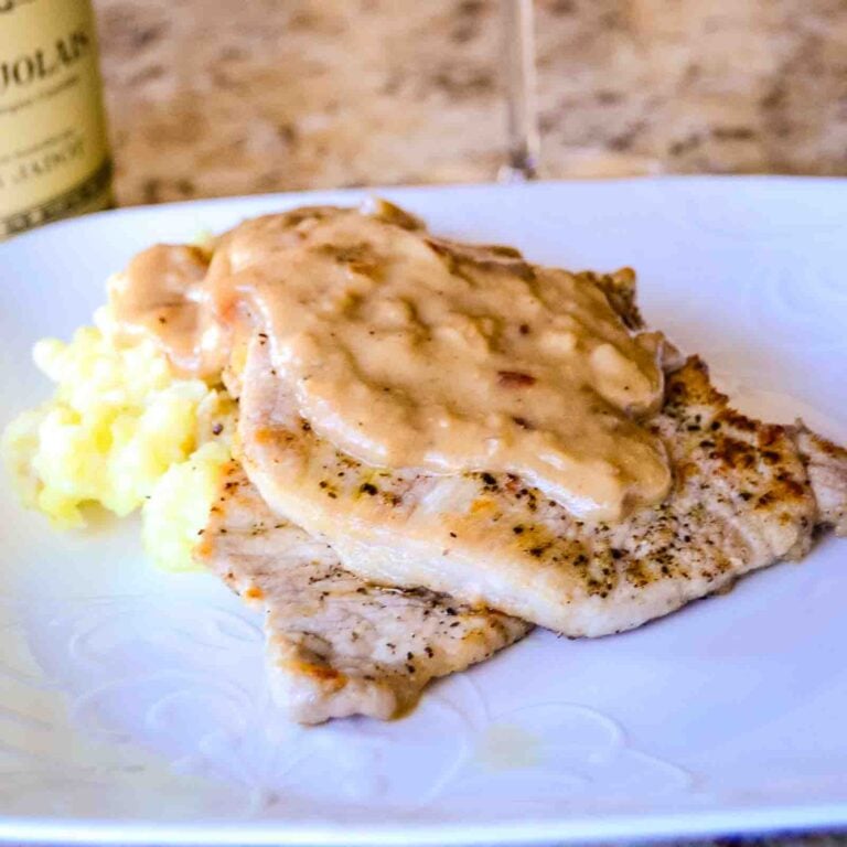 Pork chops on a white plate served on mashed potatoes with a Dijon mustard shallot gravy on top.