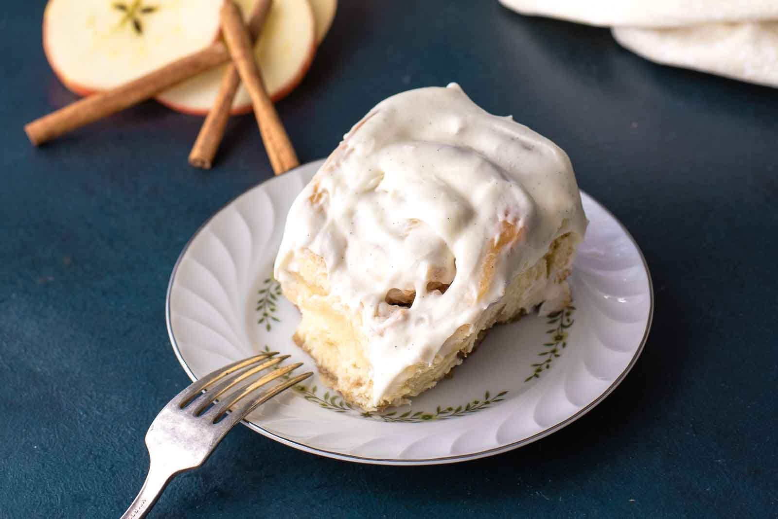 A pan of freshly baked and frosted apple cinnamon rolls on a dark blue background.