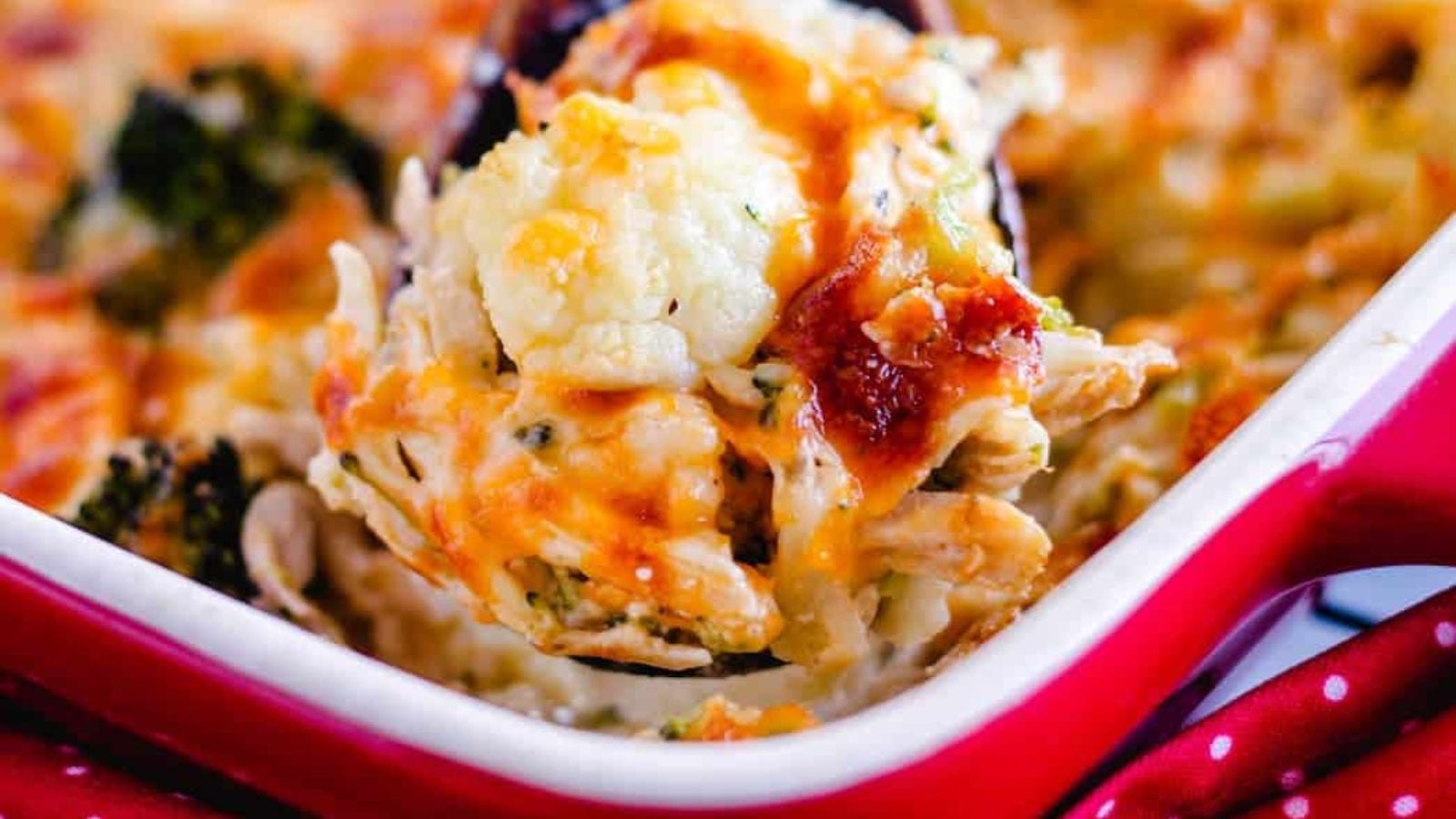 A wooden spoon scooping out a portion of cauliflower chicken casserole.