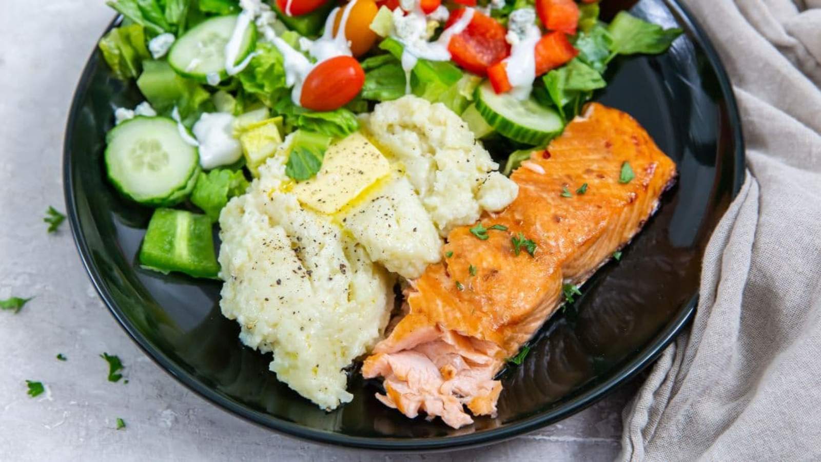 Air Fryer Teriyaki Salmon with rice, butter, parsley, black pepper, and a salad on a black plate.
