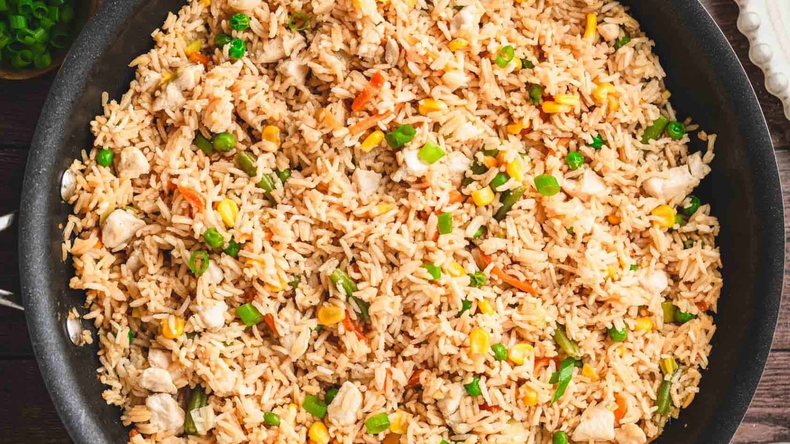 A plate of fried rice with vegetables, chicken pieces, and chopped green onions, with chopsticks on the side.