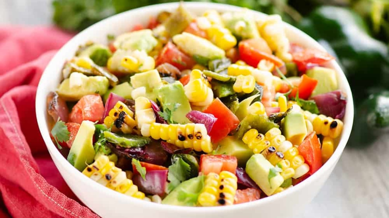 Grilled corn and avocado salad with charred corn, fresh avocado slices, and greens in a bowl.