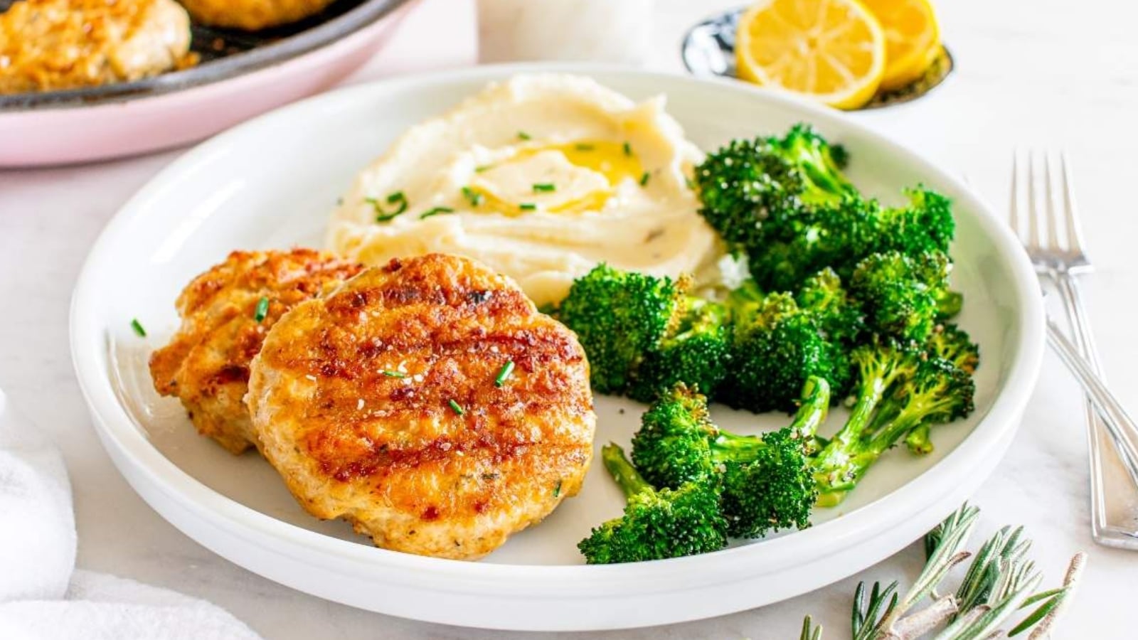 Lemon herb chicken patties served with mashed potatoes, broccoli, and a lemon wedge on a plate.