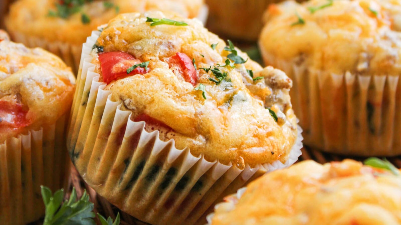 Close-up of savory muffins with herbs, tomato pieces, and cheese in white paper liners.