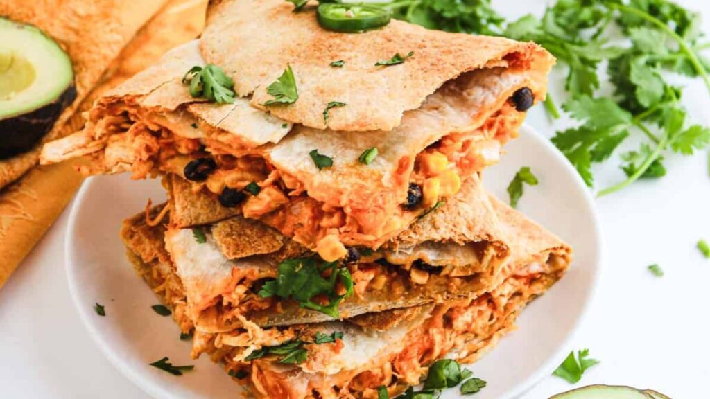 Stack of chicken quesadilla wedges with cilantro garnish.