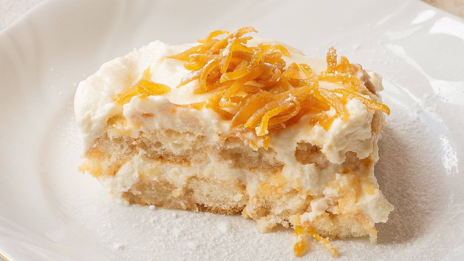A slice of creamy tiramisu topped with shredded orange zest on a white plate.