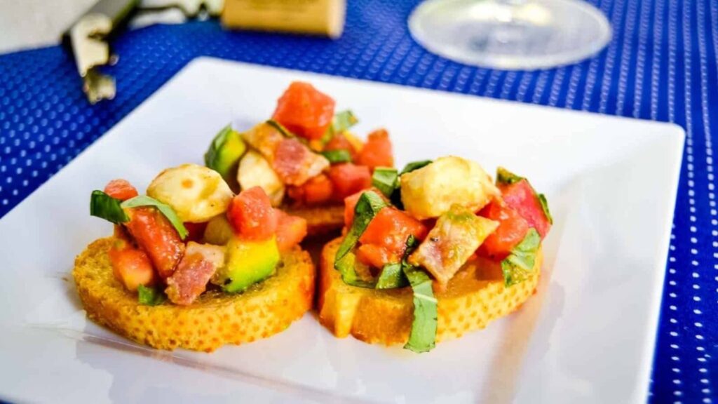 Loaded bruschetta salad on crostini on a white plate.