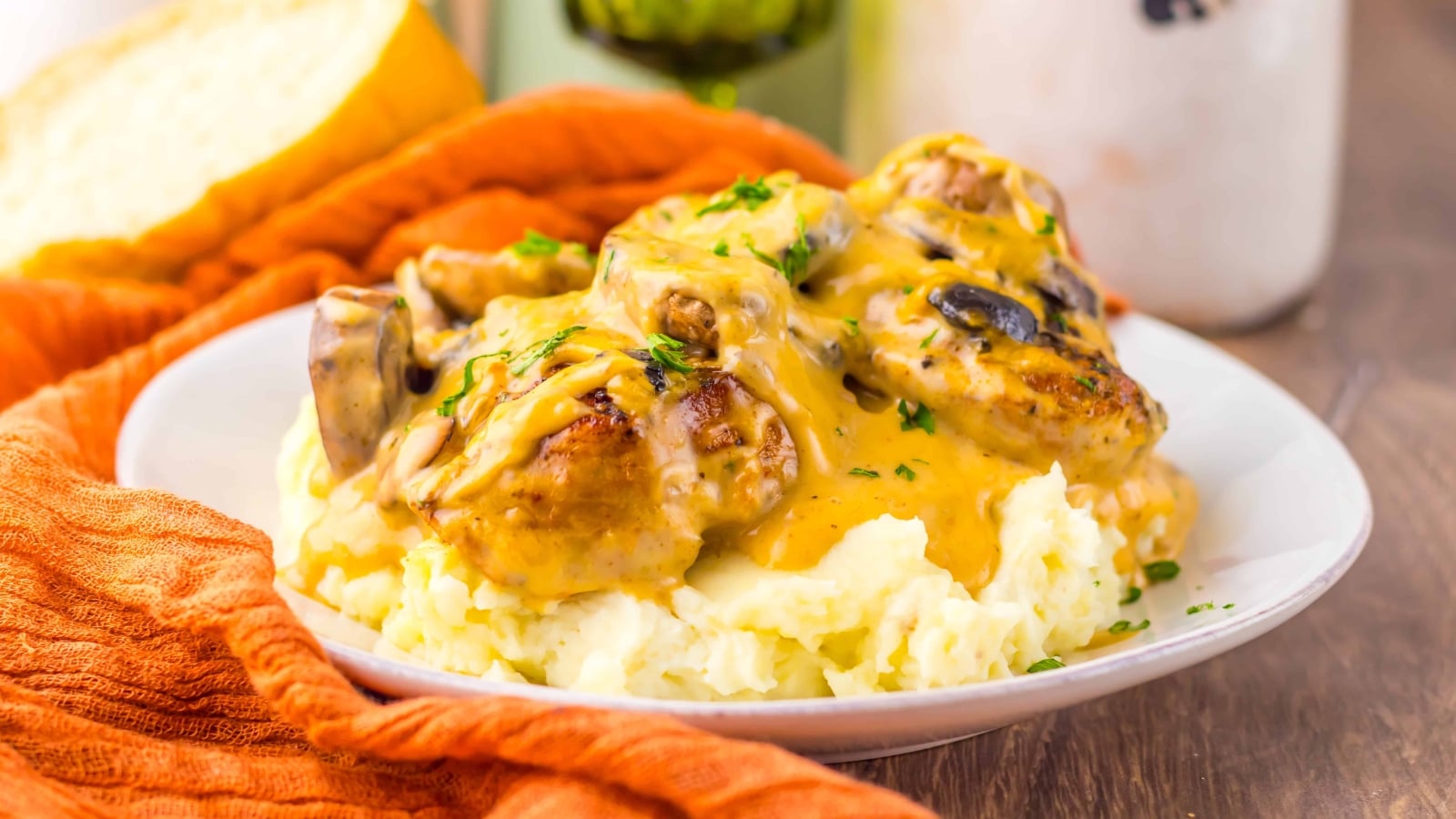Plate of mashed potatoes topped with chicken, mushrooms, and creamy gravy, garnished with chopped herbs.