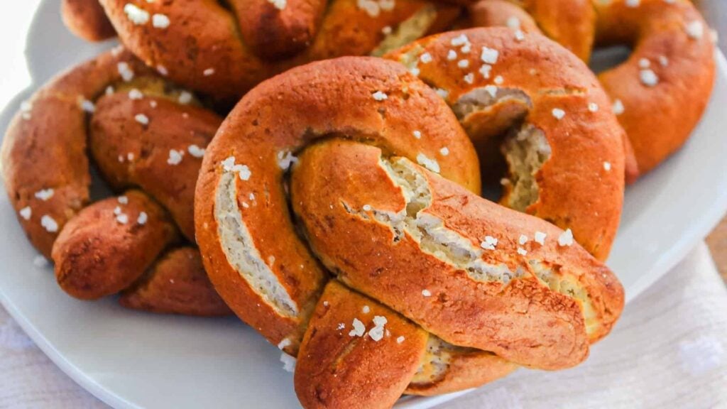 A close-up of several salted soft pretzels on a white plate.