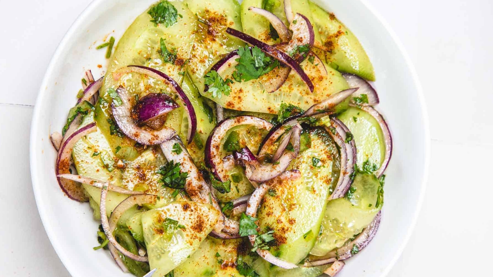 Sliced avocado and red onion salad topped with herbs and spices on a white plate.