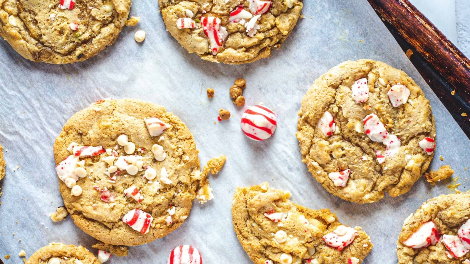 Cookies with white chocolate chips and crushed peppermint candy on parchment paper, with whole candies visible.