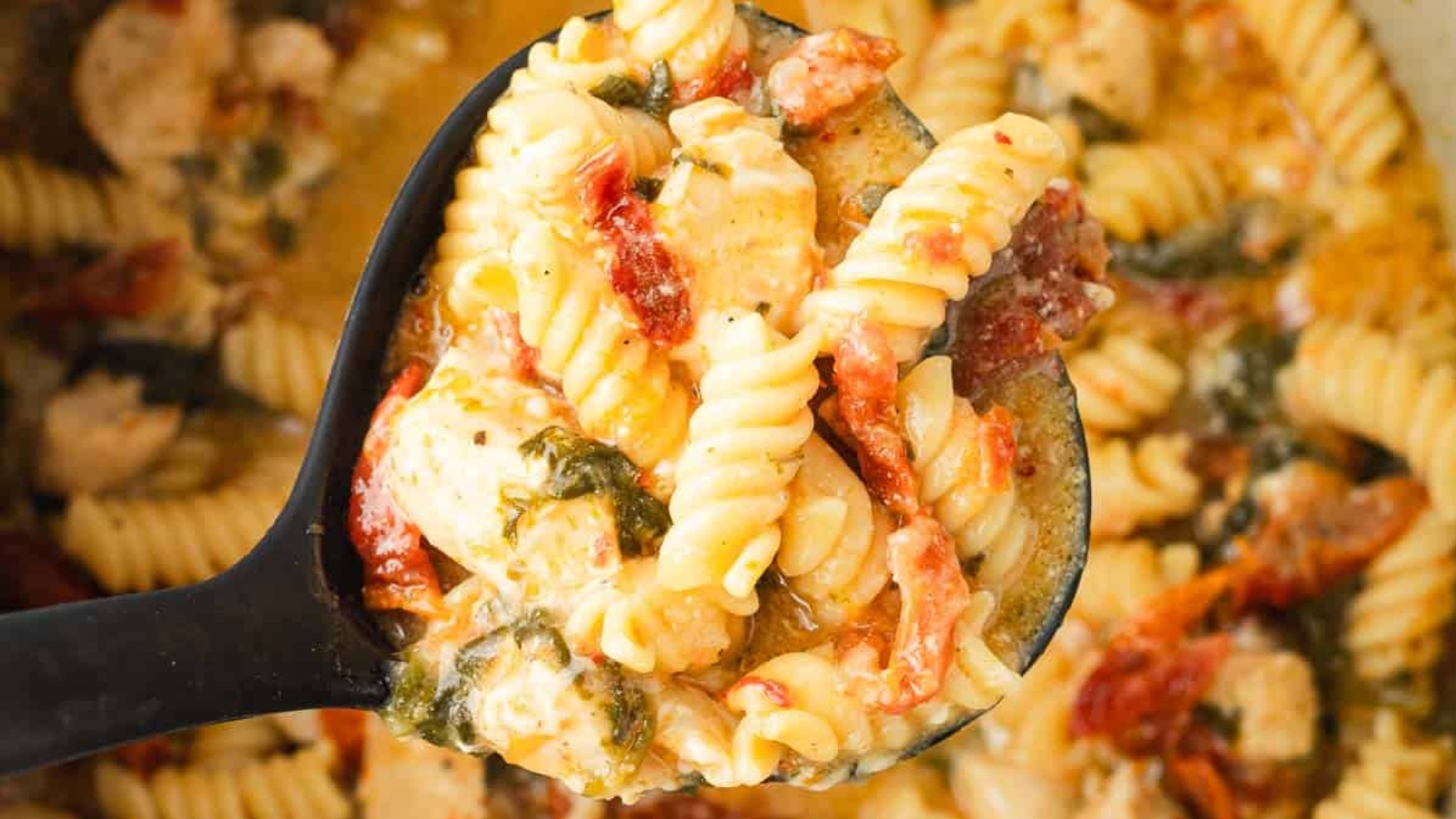 A bowl of creamy pasta with chicken, sun-dried tomatoes, spinach, and shredded cheese on top.