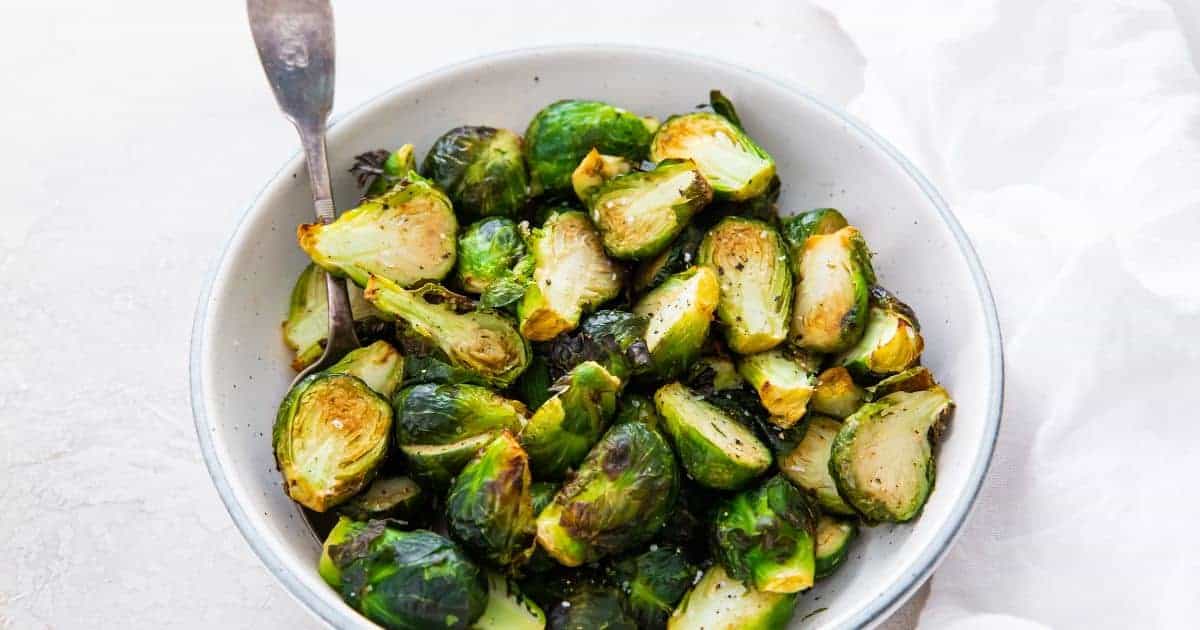 Brussel Sprouts in a white bowl with a spoon.