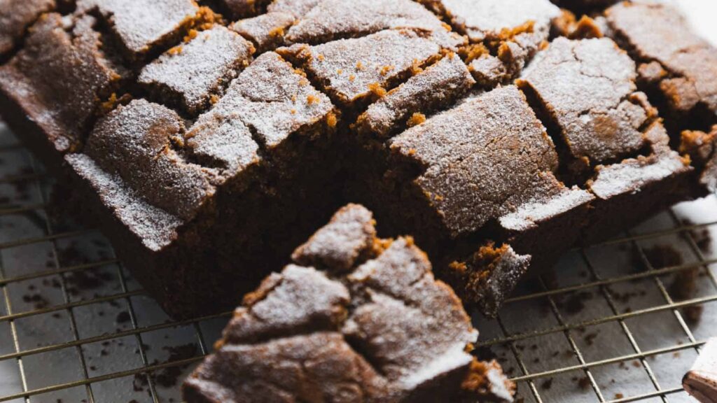 A close-up of sliced gingerbread loaf with a dusting of powdered sugar, resting on a cooling rack.