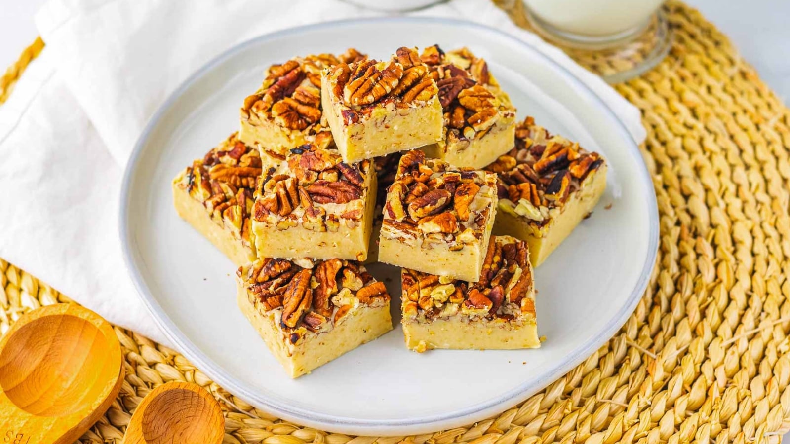 A plate of pecan-topped dessert bars stacked on a white plate, set on a woven placemat.