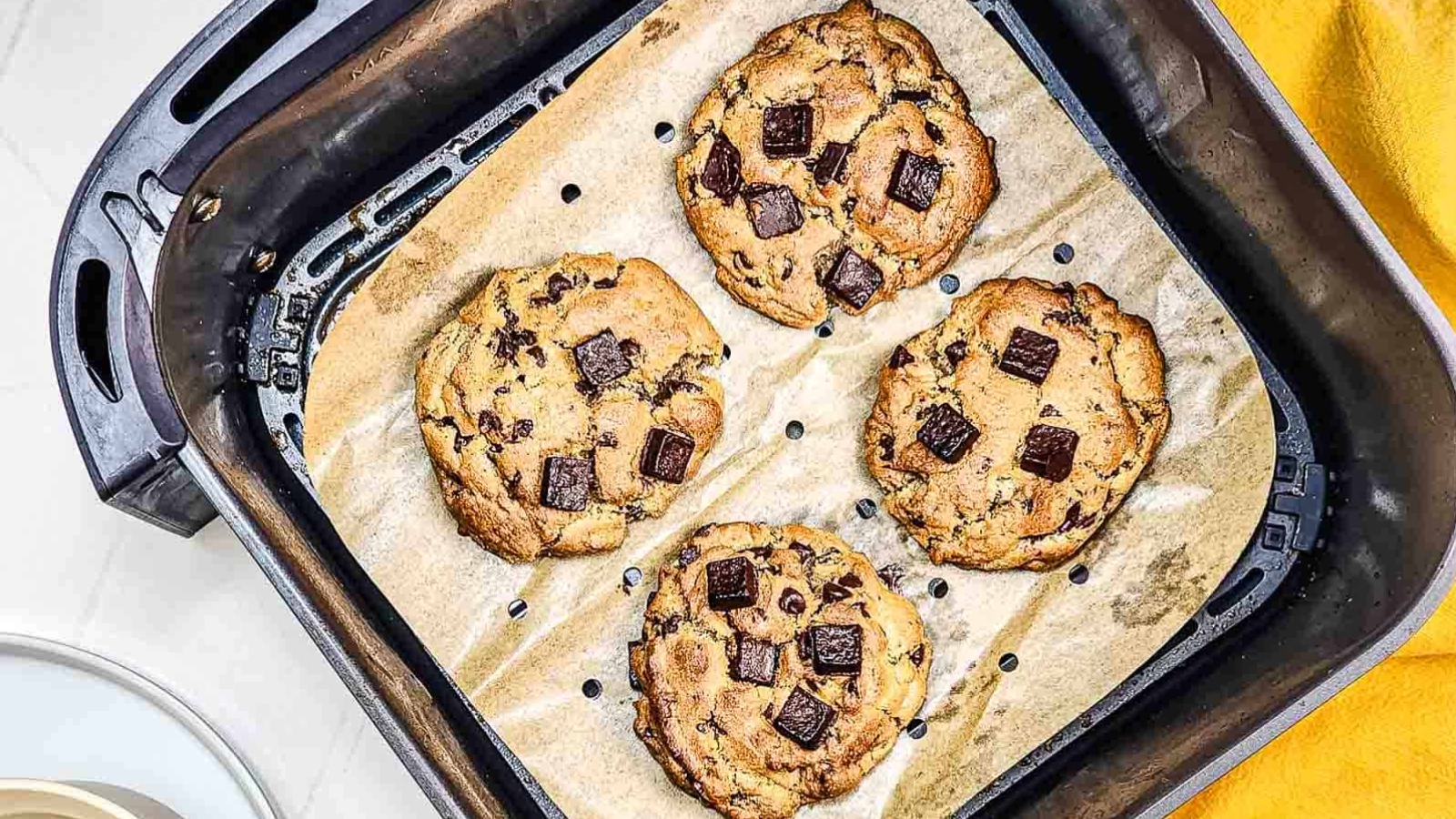 Four chocolate chunk cookies on parchment paper inside an air fryer basket.