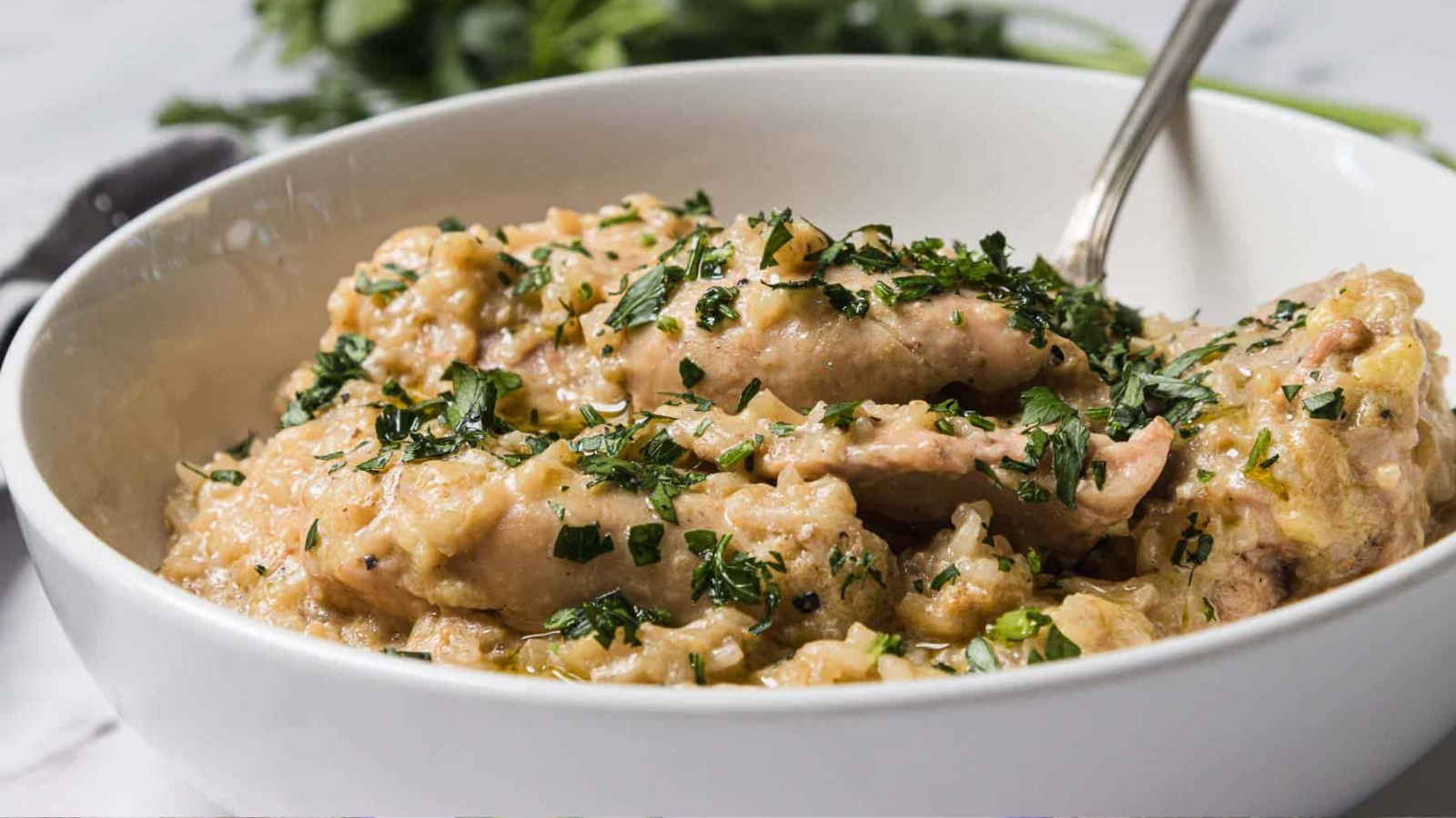 A bowl of creamy chicken stew garnished with chopped herbs and served with a spoon.