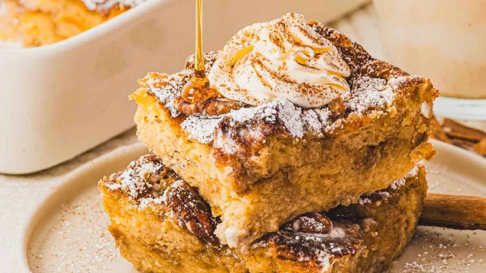 Two thick slices of bread pudding topped with ice cream, syrup, and cinnamon on a plate.