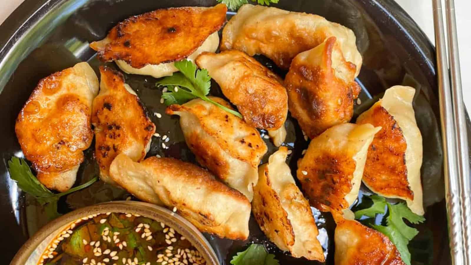 Crispy-bottom pan-fried dumplings with juicy and savory fillings on a black plate with a sauce on the side.