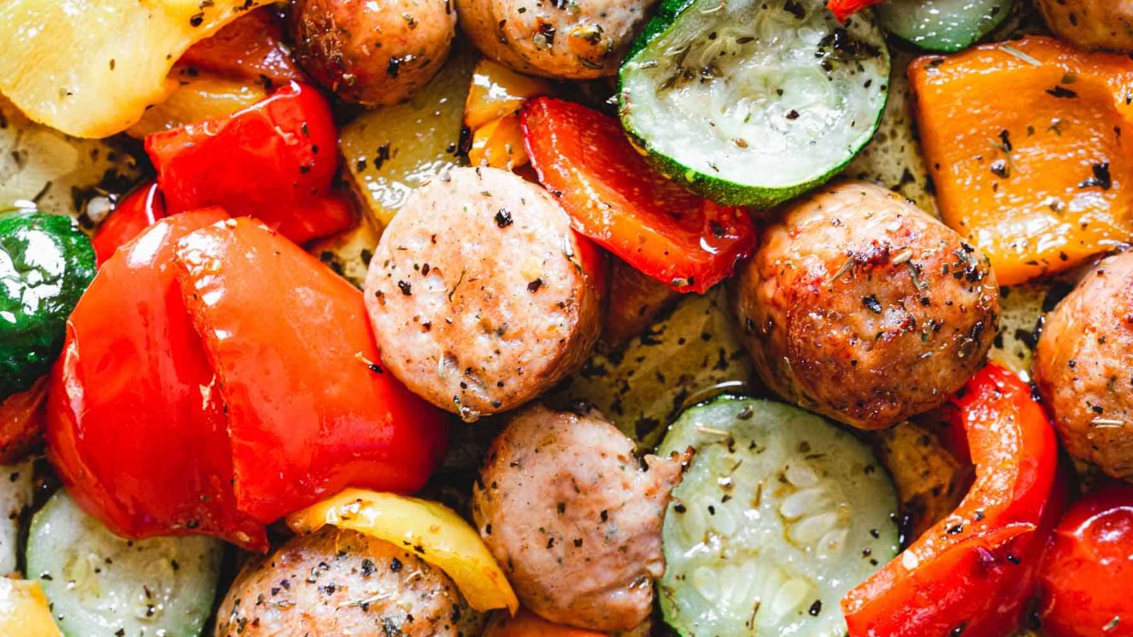 Close-up of roasted meatballs with a mix of colorful, chopped bell peppers and zucchini slices.