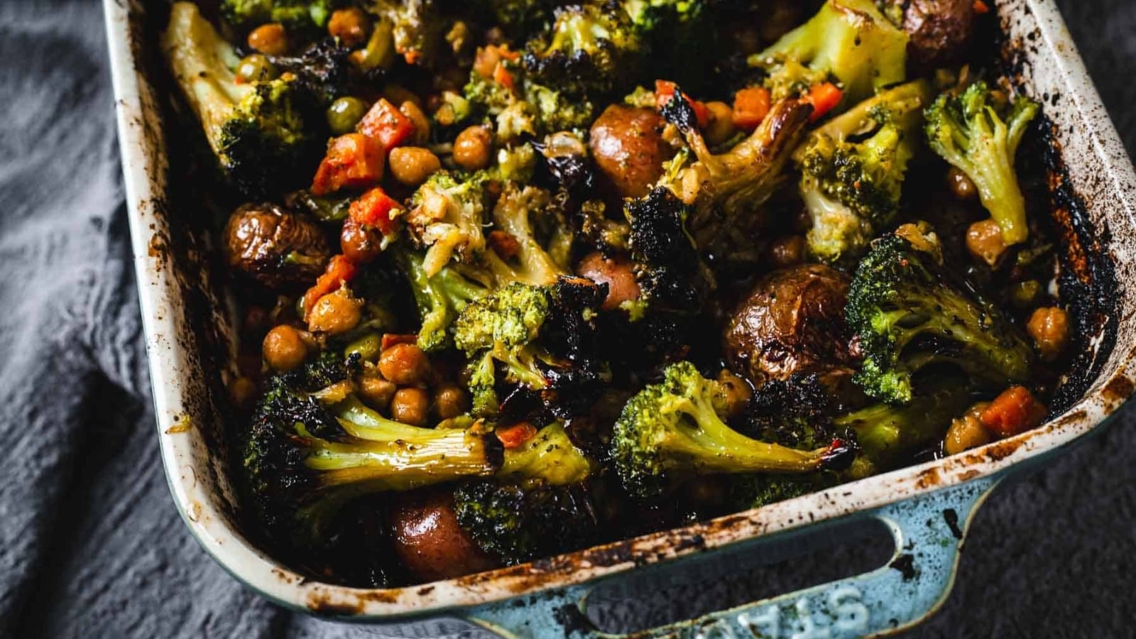 A casserole dish filled with roasted broccoli, potatoes, chickpeas, and diced vegetables.