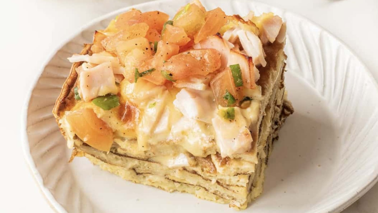 Baked casserole topped with melted cheese and chopped pieces of ham in a white rectangular dish.