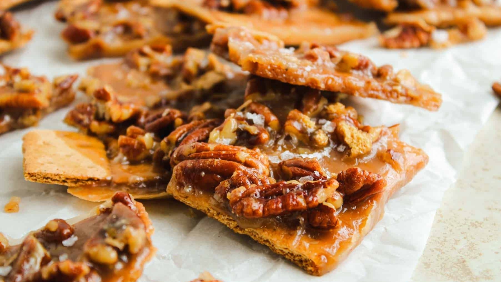 Close-up of pecan pie bark with caramelized pecans on top of graham crackers, arranged on parchment paper.