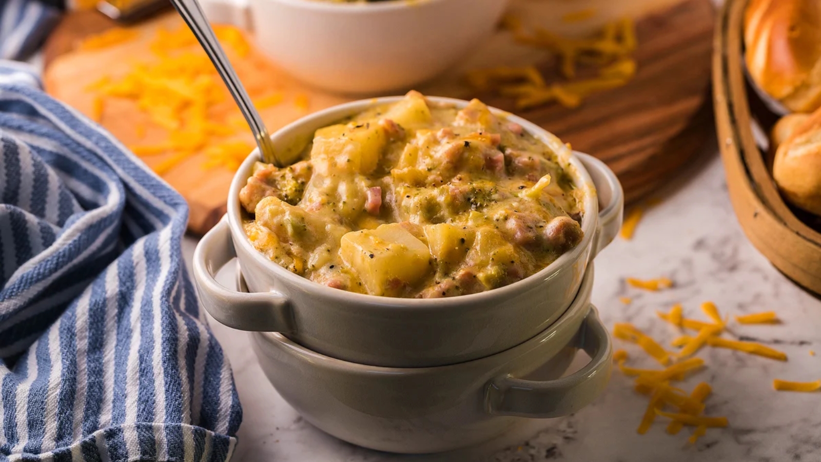 Bowl of creamy slow-cooker ham, potato, cheese, and broccoli soup garnished with cracked black pepper and chopped herbs.