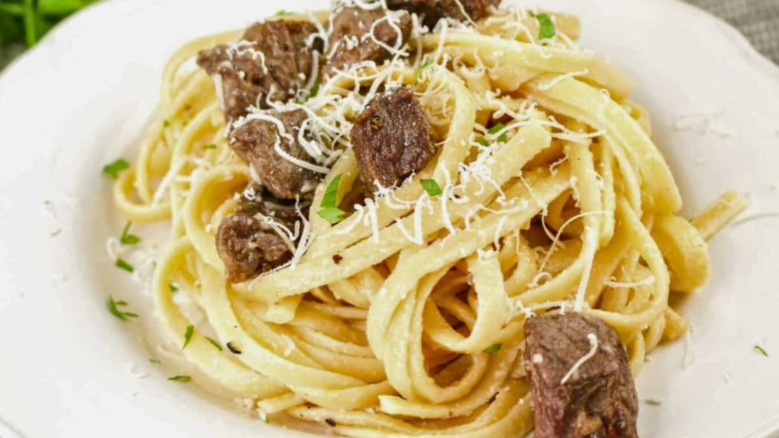 Une assiette de pâtes garnies de morceaux de viande et de fromage râpé.