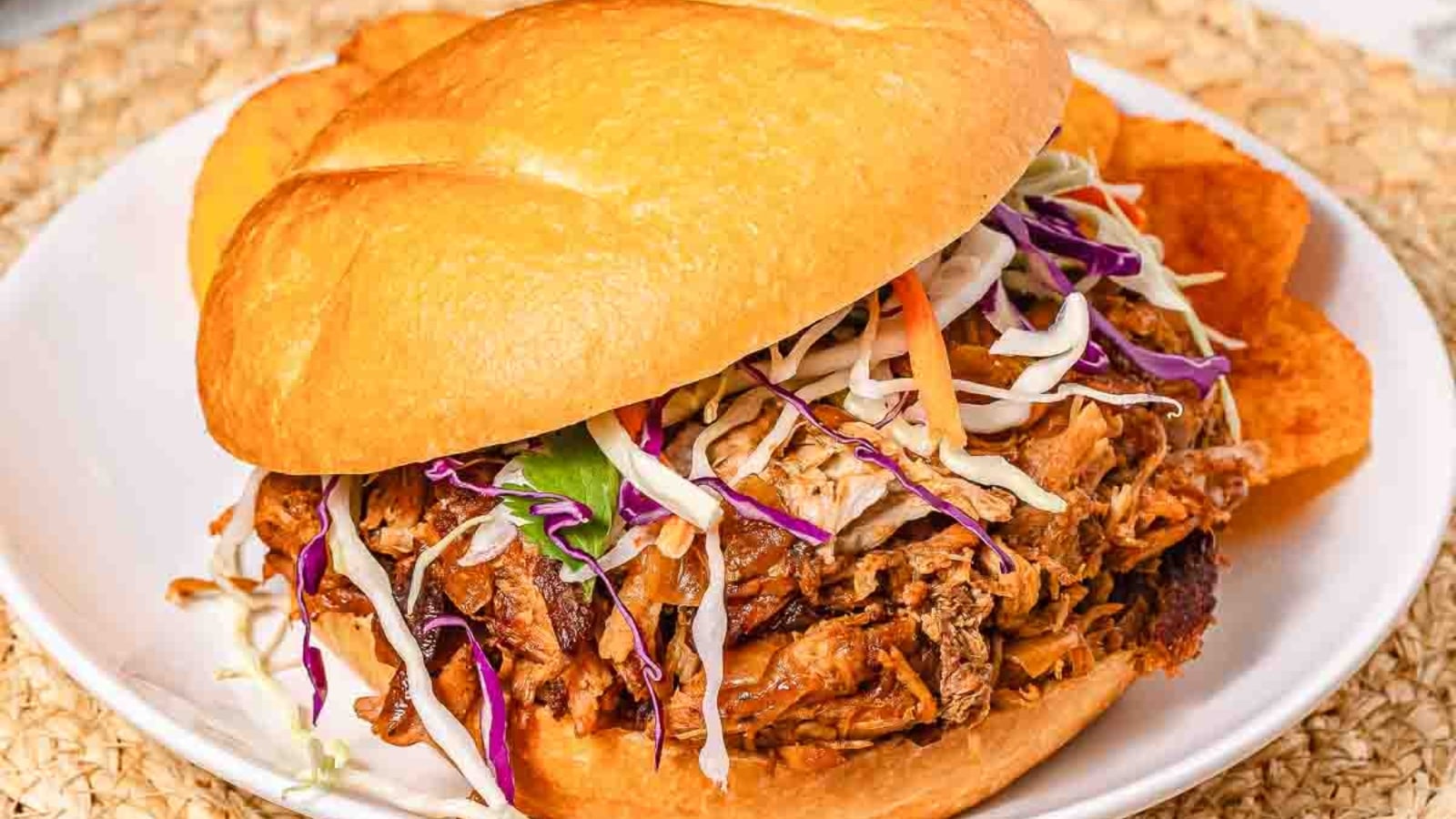 Pulled pork sandwich topped with coleslaw, served with potato chips on a white plate.