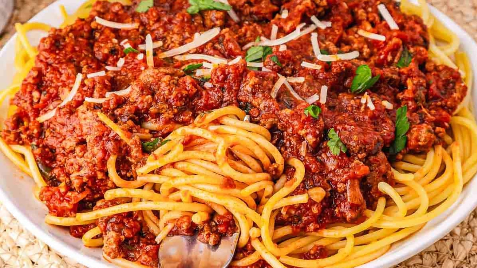 A plate of spaghetti topped with chunky meat sauce and garnished with grated cheese and parsley.