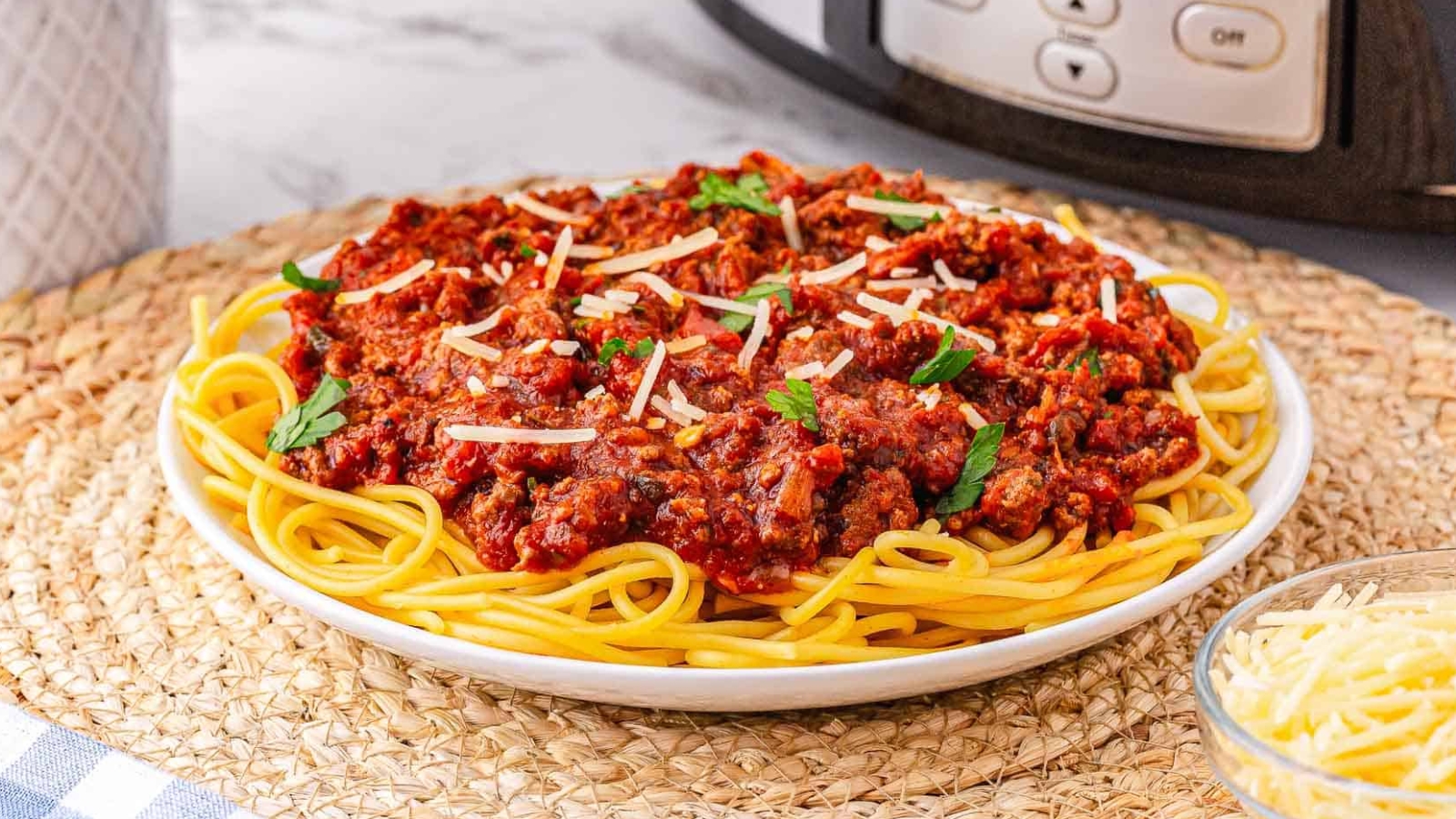 A plate of spaghetti topped with chunky meat sauce and garnished with grated cheese and parsley.