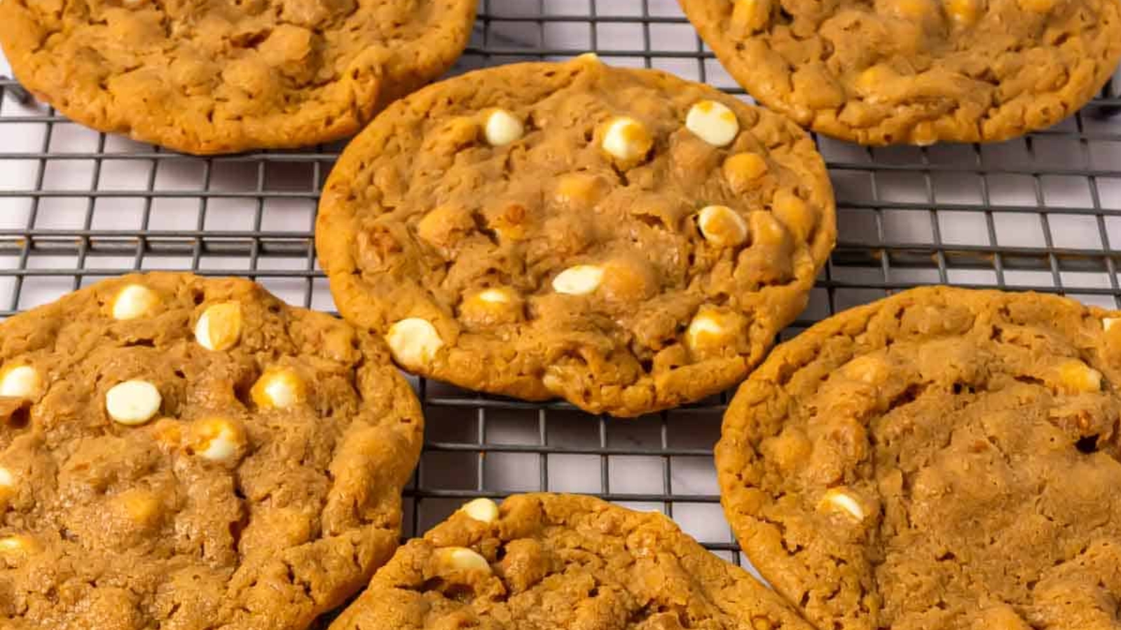 A plate of golden brown cookies with white chocolate chips, surrounded by more cookies and a textured cloth.
