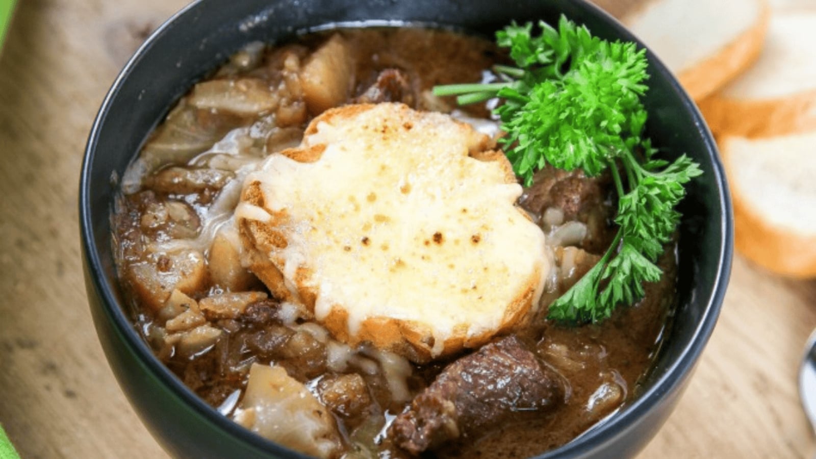 A bowl of French onion soup topped with a slice of toasted bread and melted cheese, garnished with fresh parsley.