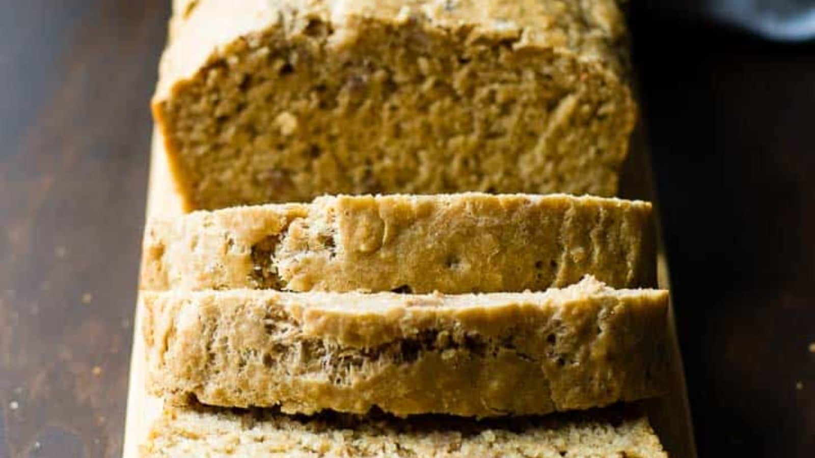 A loaf of bread with several slices cut, displayed on a wooden surface.