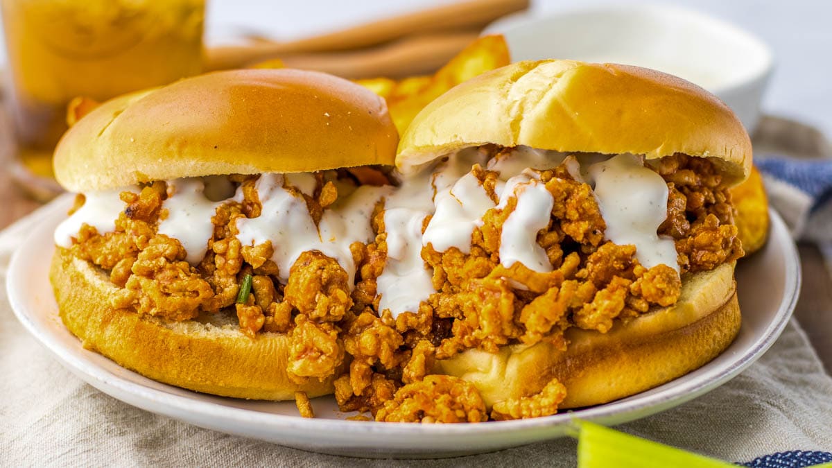 A close-up of a crispy Buffalo Chicken Sloppy Joe sandwich with creamy sauce on a soft bun, served on a plate.