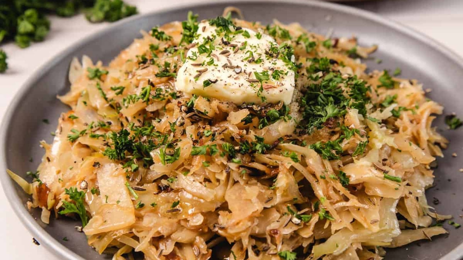 Shredded saut&eacute;ed cabbage with herbs and a pat of butter on top, served on a gray plate.