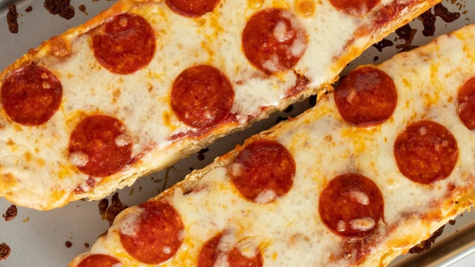 Two pieces of French bread pizza topped with melted mozzarella cheese and pepperoni slices on a baking sheet.