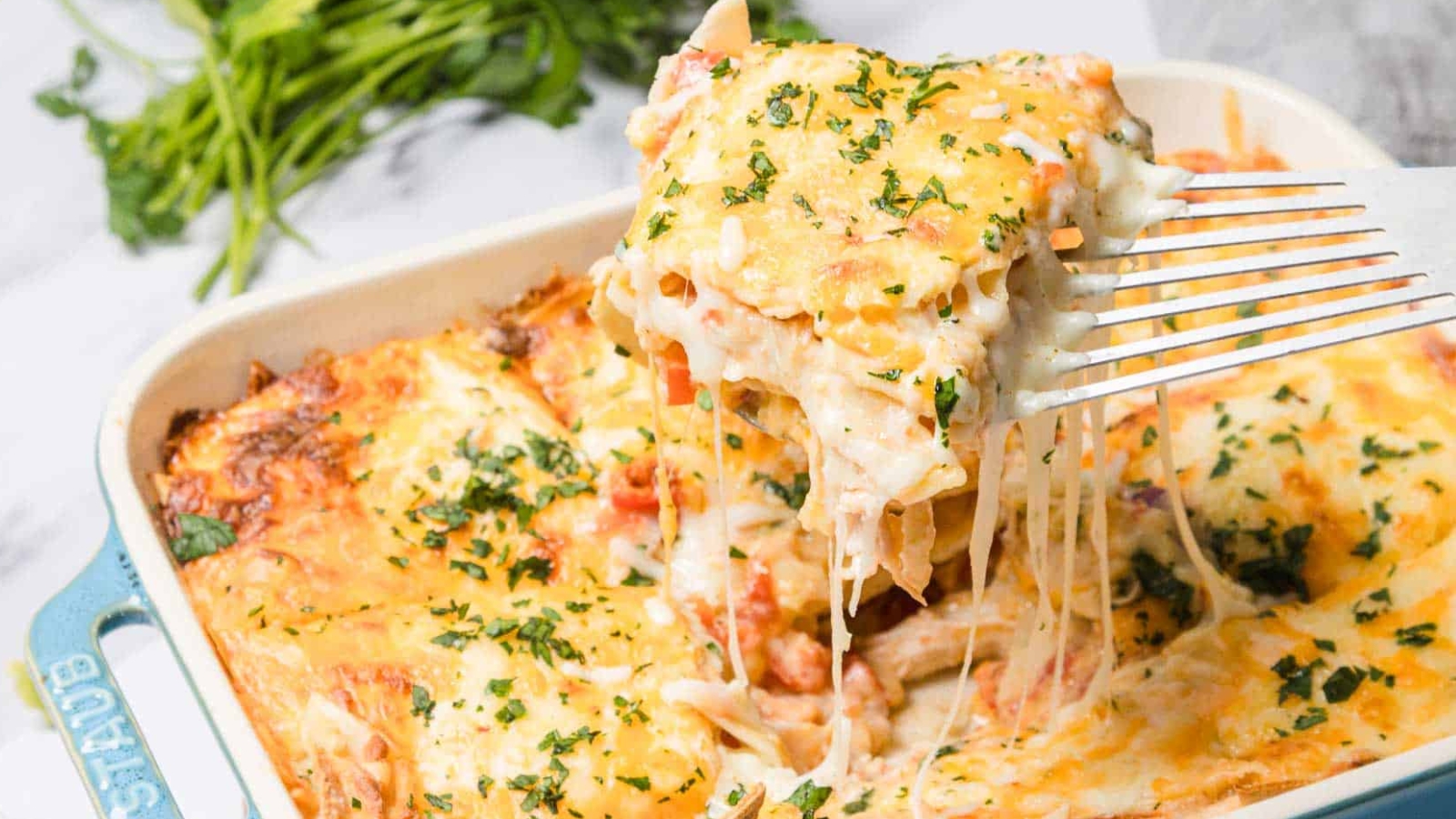 A cheesy baked lasagna in a blue dish, with a square piece removed and herbs sprinkled on top.