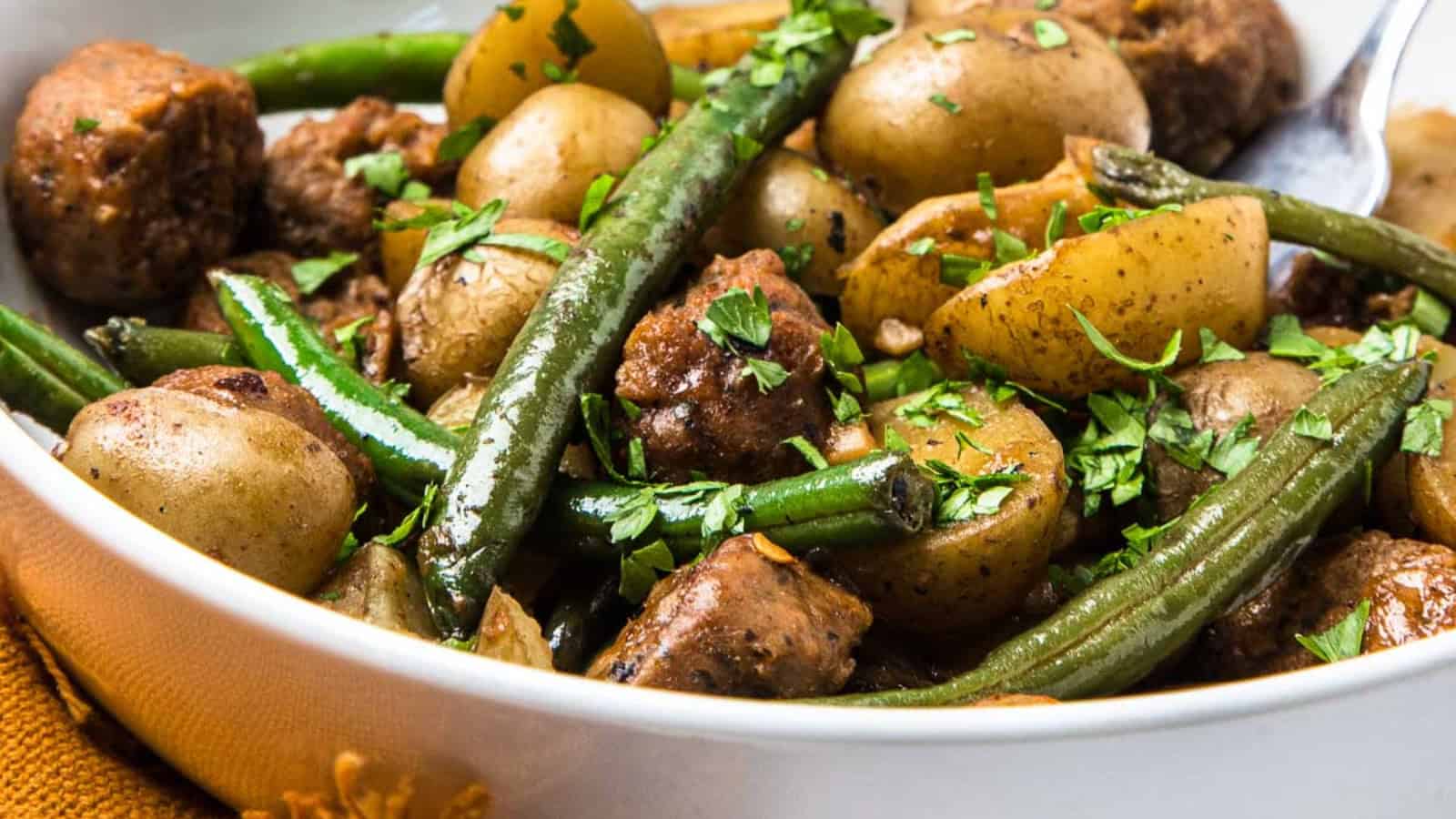 Close-up of a bowl filled with green beans, potatoes, meat chunks, and herbs.