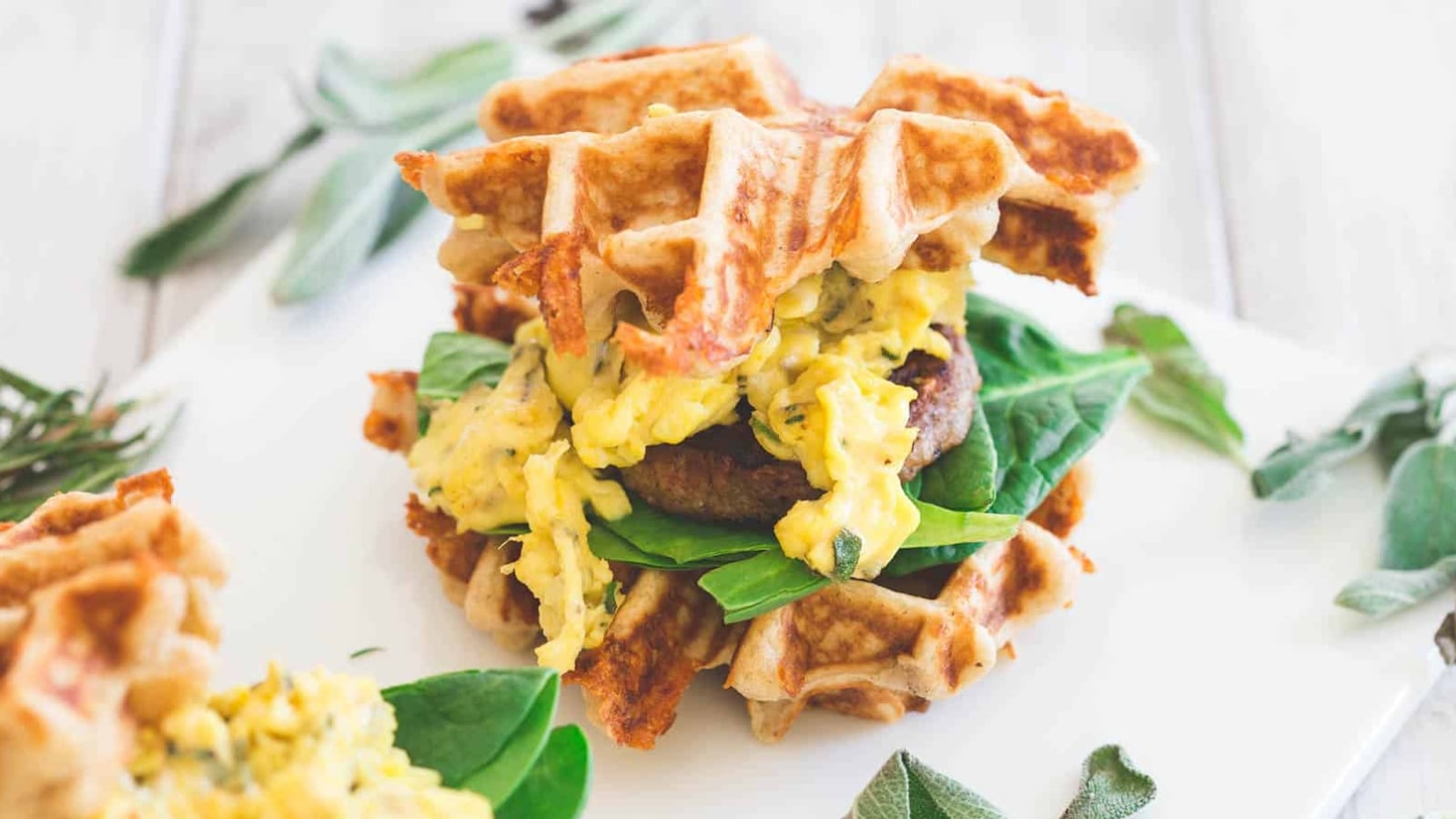 Cheddar sausage and egg waffle sandwiches with baby greens on white platter.