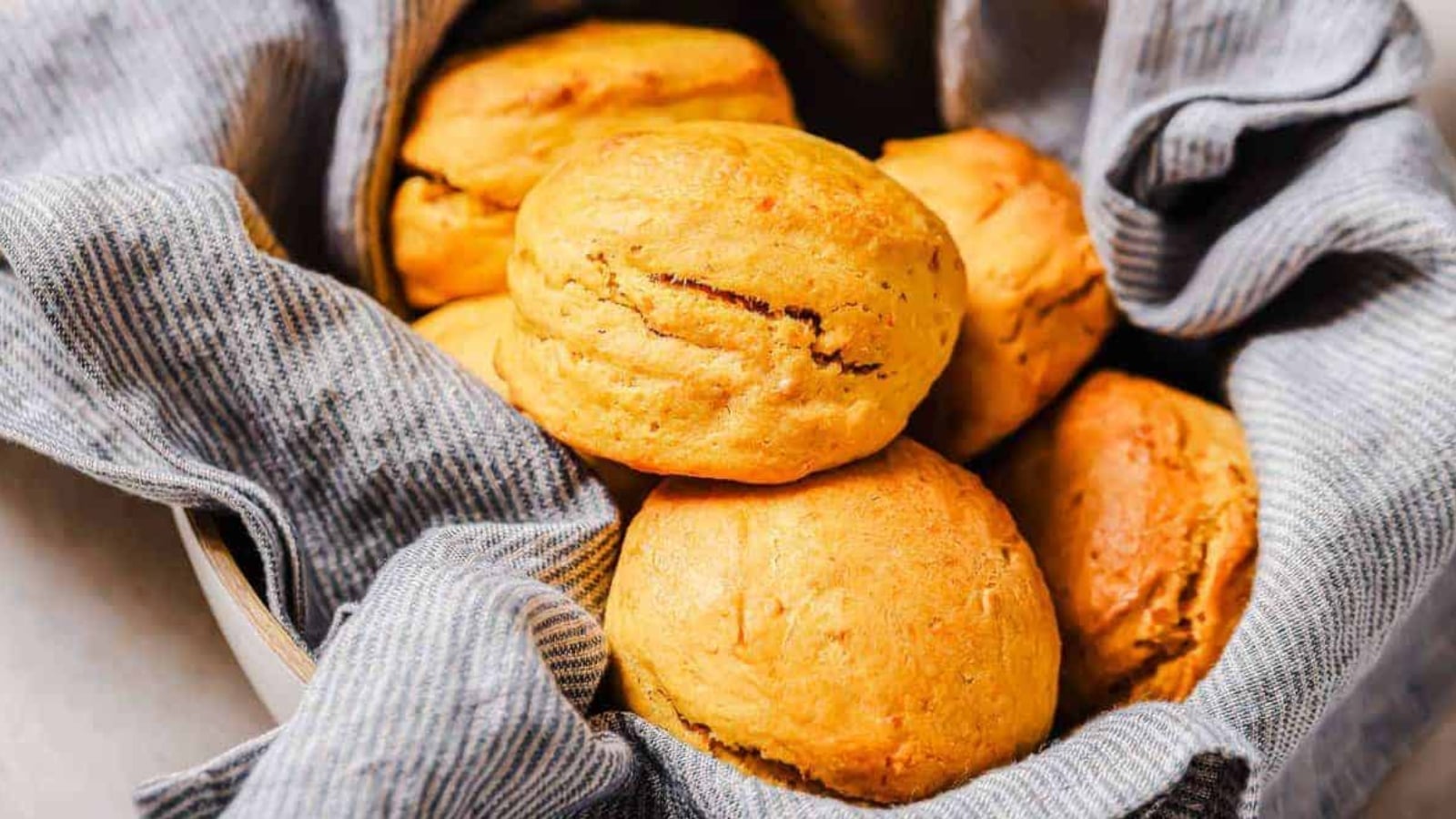 A bowl lined with a gray striped cloth holds several golden-brown biscuits.