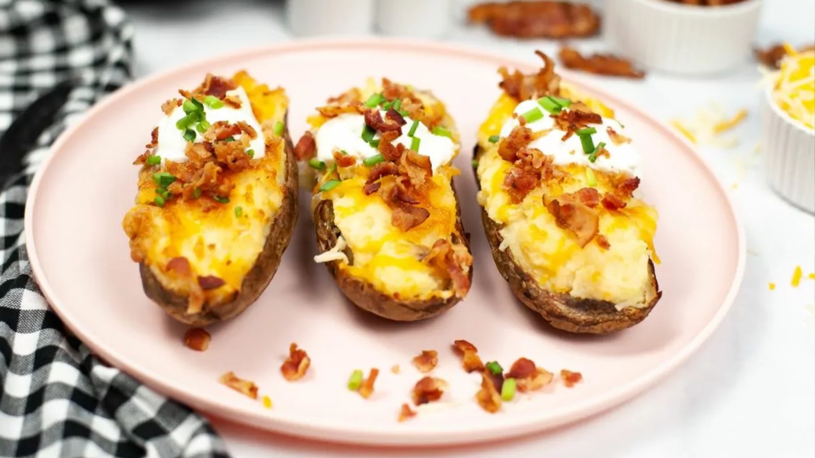 Three loaded twice-baked potato halves, a must-try for air fryer recipes, topped with cheese, bacon, sour cream, and chives on a pink plate.