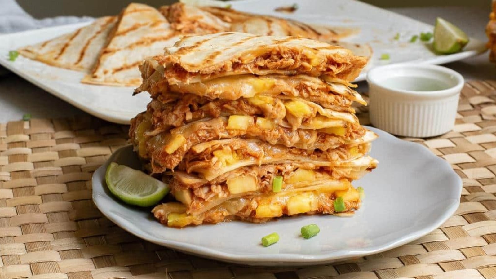 A stack of quesadilla wedges filled with shredded meat, melted cheese, and pineapple on a gray plate, garnished with a lime wedge.