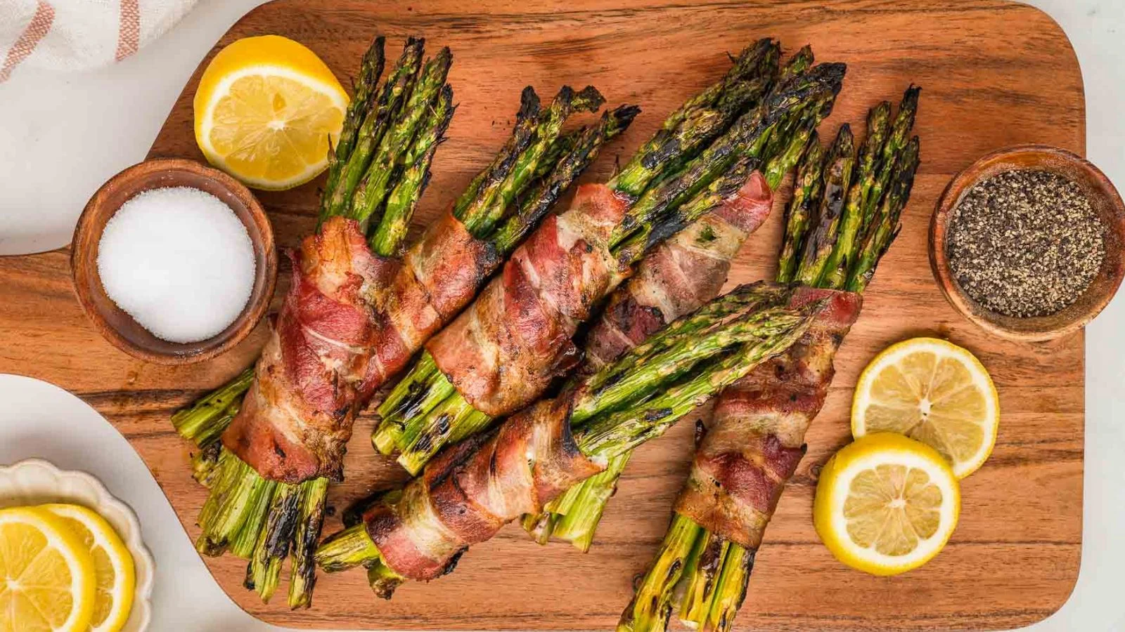 Grilled bacon-wrapped asparagus spears with crisped edges arranged on a platter.