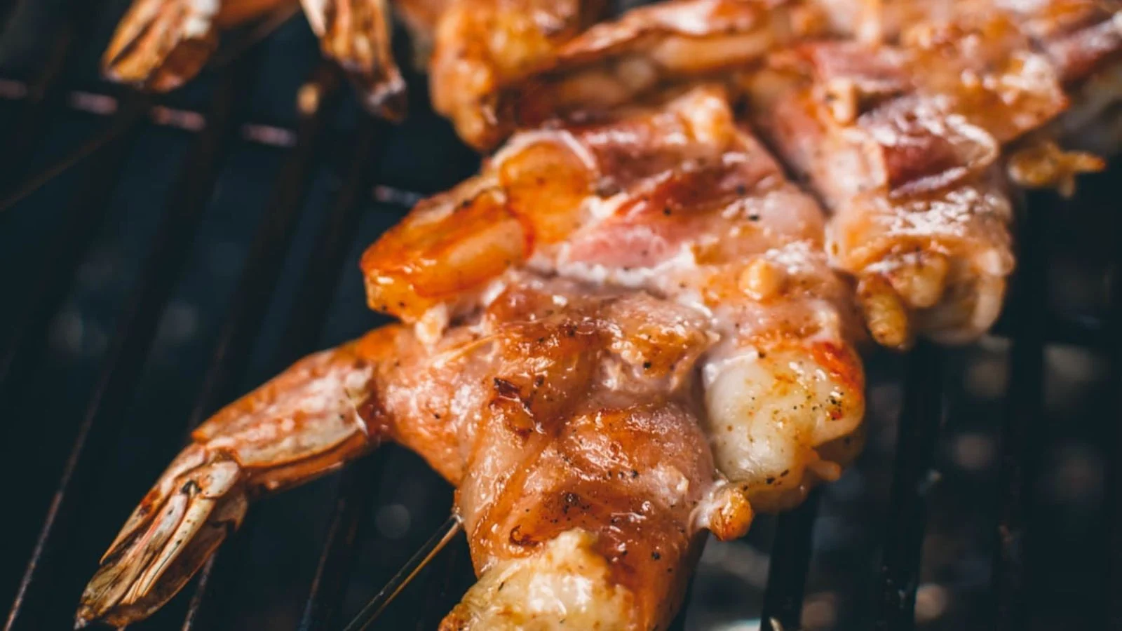 Grilled bacon-wrapped shrimp with crisped bacon exterior plated next to dipping sauce.