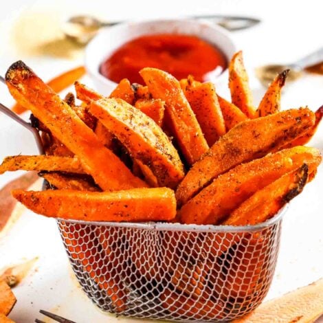 Crispy air fryer sweet potato fries piled in a metal serving basket with sweet and spicy sriracha sauce for dipping.