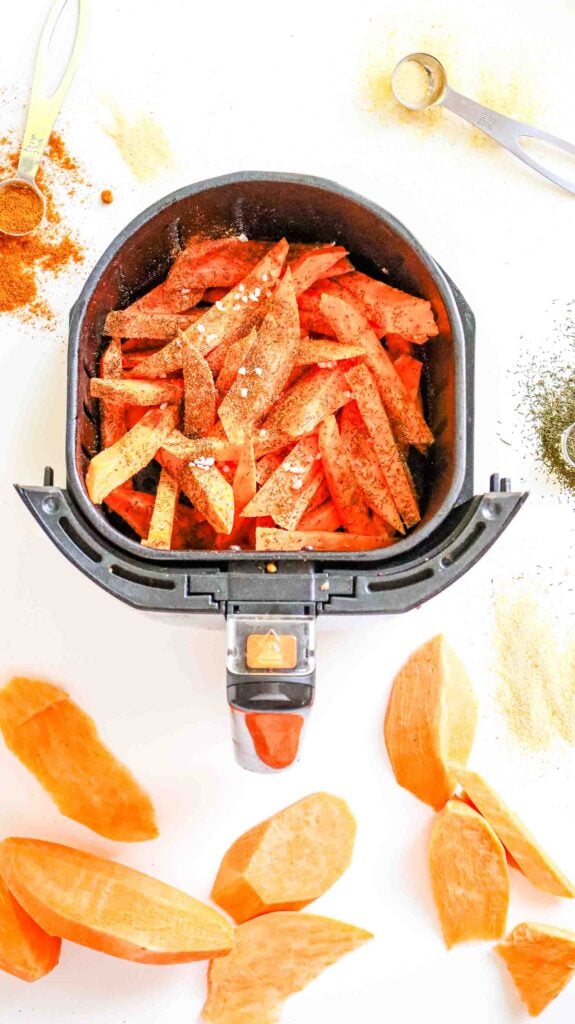 Seasoned raw sweet potato strips arranged in a single layer in an air fryer basket.